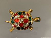 Top view of gold tone turtle brooch showing multicolour enamel and rhinestones