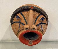 Front view of round terracotta mask showing facial features and painted details