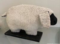 Full profile of sheep showing curly faux-fur body, black head, wood base