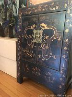 Front view of the black cabinet featuring gold painted dragons, metal hardware on doors, and decorative border patterns.