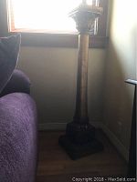 Full view of the tall wood pedestal placed next to a sofa, showing its height and rectangular base.