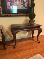 Full view of the walnut side table with glass inset and a decorative plant on top.