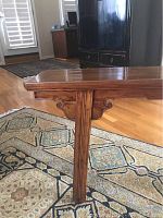 Side view showing bench top, detailed shaped apron, and straight wooden leg with natural wood grain and varnished finish.