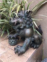 Close-up of a single foo dog statue on tiled ledge showing patina finish and openwork sphere.