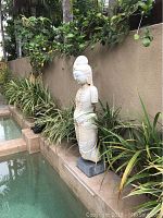 Full front view of granite Quan Yin statue standing on base beside pool