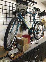 Side angle view of blue Timberline mountain bike with knobby tires, water bottle holders, and front handlebar bag, shown indoors on a cabinet.