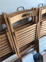 Stacked wood folding chairs showing the top backrests and folded seats in natural finish.