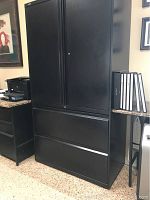 Front view of closed black metal file cabinet showing tall rectangular shape with two doors on top and two drawers below