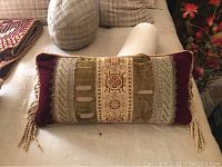 Front view of antique bolster style pillow with velvet fabric and bullion fringe, showing burgundy and olive green tones with embroidered center.