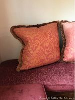 Pair of decorative rectangular pillows with a red-orange and gold pattern, fringed edges, on a reddish couch.