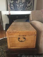 Front and side view of rectangular antique leather trunk showing brass side handle and leather panel stitching detail.