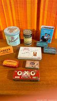 Group of ten vintage tins and one cardboard box displayed on table