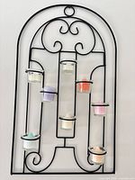 Full frontal view of black metal arched sconce with eight votive cups