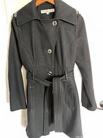 Front view of black wool coat on hanger showing buttons, belt, pockets, epaulettes