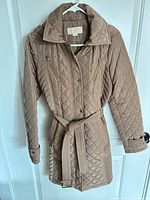 Front view quilted beige/taupe coat on hanger showing belt, quilting, gold-tone zippers