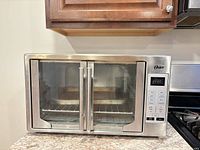 Front view of Oster stainless steel convection toaster oven with closed French doors and control panel visible