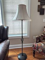 Full view of black metal floor lamp with cream bell shade and beaded fringe