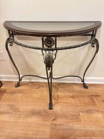 Front view of demilune console table showing wrought iron frame, wood trim, glass top