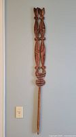 Full view of carved wooden staff hanging on wall
