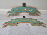 Two bronze ribbon banner panels with gold lettering and central steel mounting tab