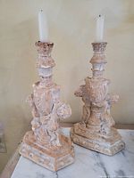Two distressed ceramic candlesticks with cherub designs