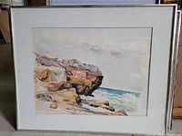 Framed watercolor painting showing rocky coast and surf under glass