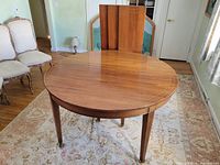 round mahogany veneer table with leaves standing behind, shown on rug