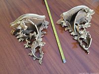 Pair of ornate gilded wall shelves with tape measure for scale
