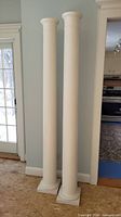 Two white unfinished pine columns standing side by side showing full height, capitals and bases