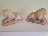 Both alabaster lion figurines shown from side profile on shelf