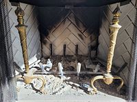 Pair of cast brass andirons installed in fireplace showing twisted columns, flame finials, paw feet, and iron support bars