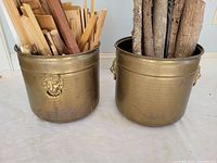 Two hammered brass buckets with lion head ring handles filled with wood, showing size and patina