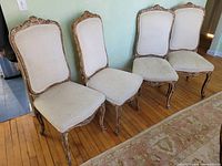 Four matching carved wood dining chairs with distressed finish and light upholstery