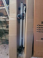 Full view of folded mechanical drafting arm inside cardboard sleeve showing aluminum rails, angle head and mounting brackets