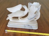 Full view of carved alabaster swan planter showing sculpture details, vase opening, base and tape measure for scale