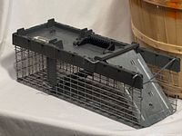 Side view of Havahart model 1026 small animal trap showing wire mesh body, spring-loaded triangular door, and top handle
