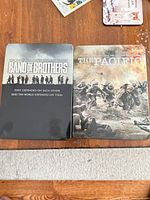 Front view of Band of Brothers and The Pacific metal collector tins on table