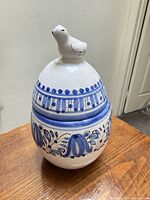 Front view of egg-shaped trinket box with bird finial, showing blue floral decoration