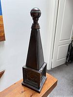 Full view of dark wooden obelisk on table
