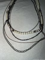 Full view of five-strand necklace laid flat showing pearls and mixed chains