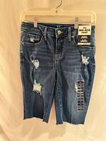 Full view of front of denim shorts on hanger showing length, rips, frayed hems, tag attached