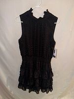 Full view of black sleeveless ruffle mini dress on hanger
