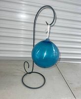 Full view of blue glass ball hanging from wrought iron stand