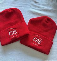 Two identical red knit cuffed beanies with CDS embroidery front view