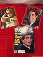 Three magazines laid out on red cloth: two Time, one People