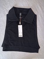 Front view of folded black ribbed collared cropped top with tag