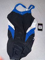 Front view of black, blue, white Nike one-piece swimsuit with racerback straps and chest swoosh, tags attached