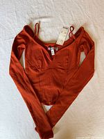 Front view of burnt orange ribbed long sleeve cropped top with straps and tags