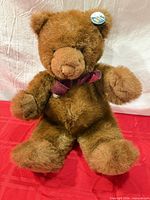Full view of brown plush Gund Truffle teddy bear seated on red cloth