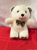 Front view of white plush teddy bear showing corduroy ears, bow tie, paw pads